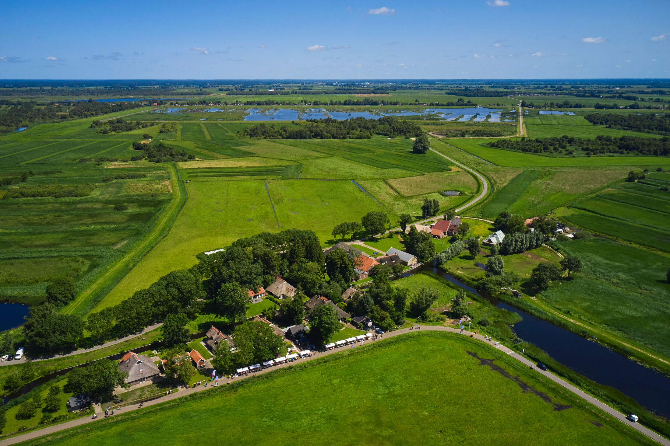 vogel perspectief foto van landschap met bomen en op voorgrond witte kraampjes met mensen op een lange strook weg