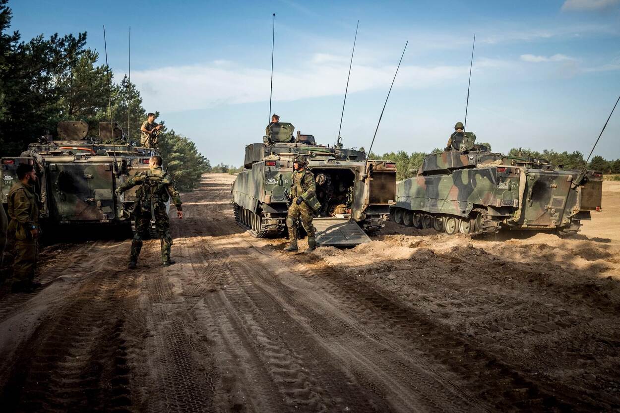 Mensen in militair kostuum op modderige grond met tanks